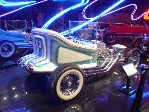 1968 Ford Mustang - A custom hot rod with a unique body style and exposed engine is displayed under neon lights, with other vehicles visible in the background.