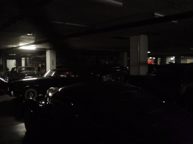 Several vintage cars parked in a dark garage, some with headlights on