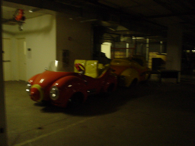 Red and yellow cartoon cars parked indoors. One car is in the foreground, the other behind it
