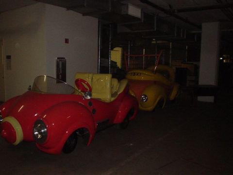 1968 Ford Mustang - Two colorful amusement park ride cars are parked indoors, one red and one yellow with 'TAXI' visible on its side.