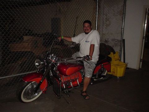 1968 Ford Mustang - A man sits on a red motorcycle parked behind a chain-link fence.