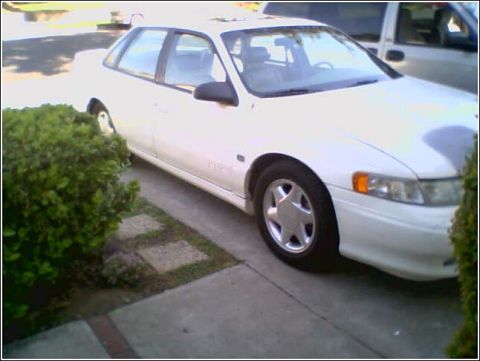 1993 Ford Taurus - A white sedan is parked on a concrete driveway next to a green bush.