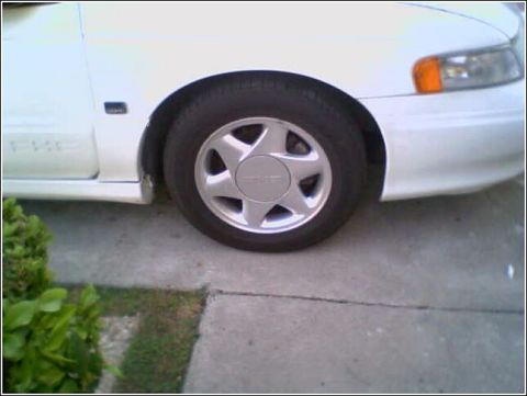 1993 Ford Taurus - A close-up view of the front wheel and fender of a white 1993 Ford Taurus.