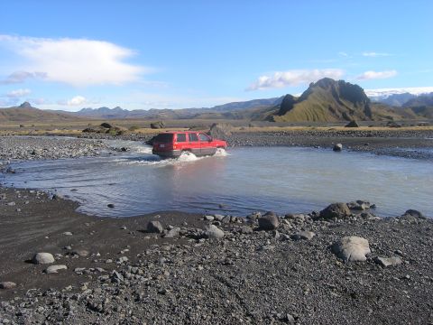 2001 Jeep Wrangler - A red SUV navigates a water crossing in a , remote terrain under a clear blue sky.
