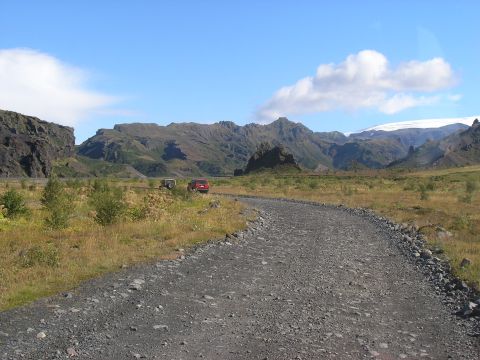 2001 Jeep Wrangler - Two SUVs drive on a gravel road through a valley with mountains under a clear blue sky.