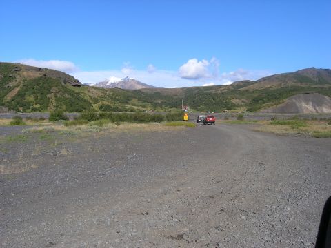 2001 Jeep Wrangler - A red SUV tows a trailer along a gravel road, set against a backdrop of rolling hills and a snow-capped mountain under a clear blue sky.