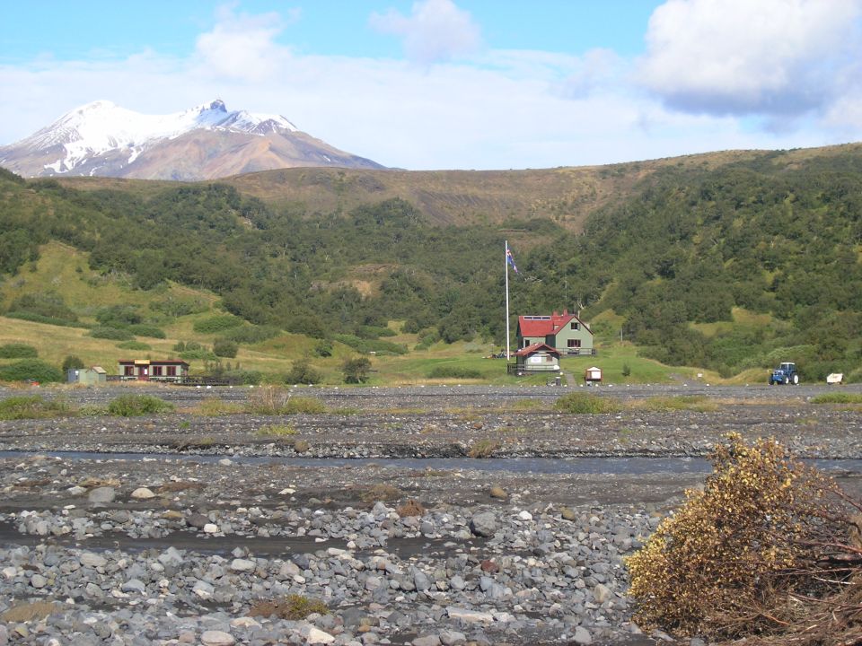 Rural scene with snow-capped mountain, buildings, and a blue tractor in the distance