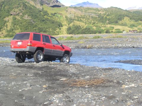 2001 Jeep Wrangler - A red Jeep Grand Cherokee navigates a rocky terrain near a flowing river.