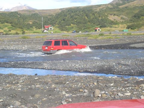 2001 Jeep Wrangler - A red 2001 Jeep Grand Cherokee navigates a rocky riverbed in a scenic, mountainous landscape.