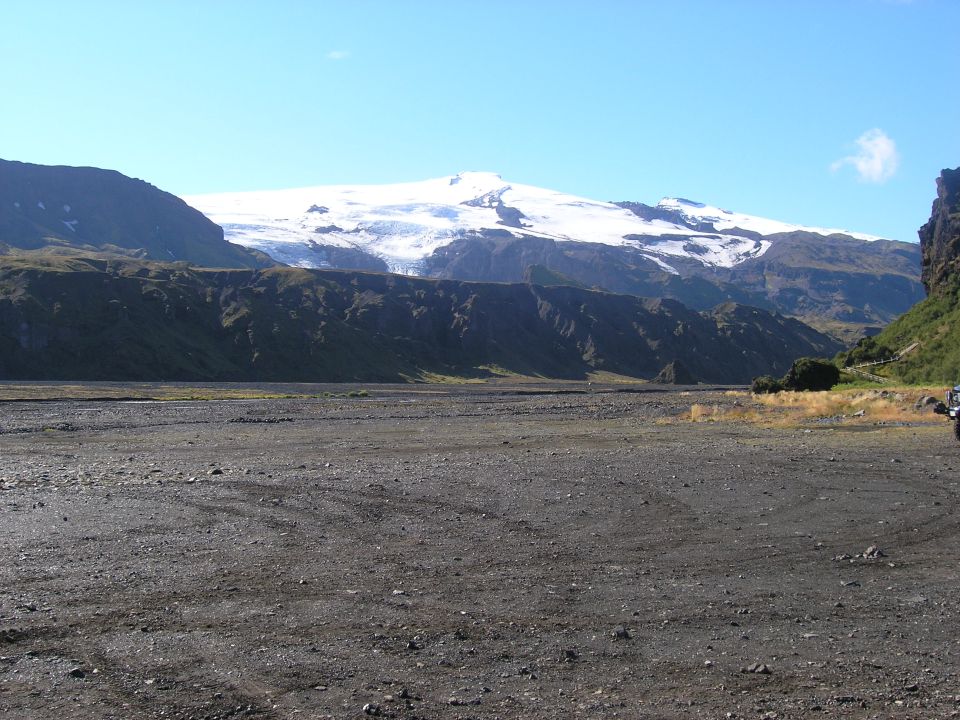 Off-road vehicle parked in a rocky, barren landscape with a snow-capped mountain range in the background