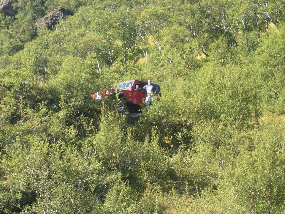 Red 2001 Jeep TJ parked on a hillside, person standing beside driver's door
