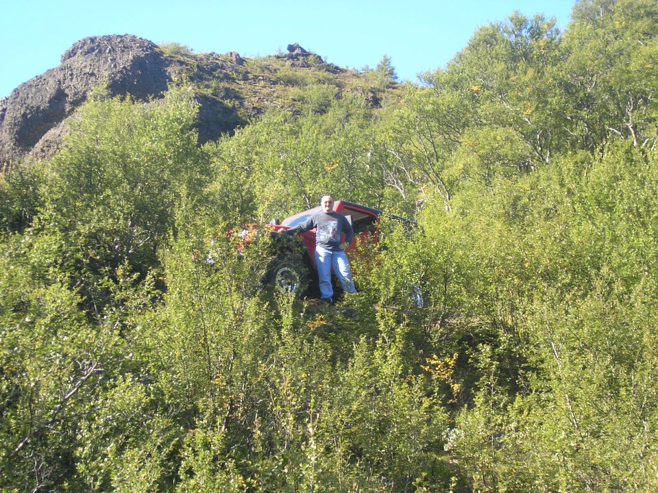 guy standing next to red off-road vehicle stuck in trees on a hill