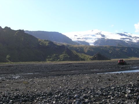 2001 Jeep Wrangler - A red SUV navigates a rocky riverbed with a snow-capped mountain range in the distance.