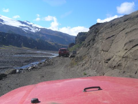 2001 Jeep Wrangler - Two red SUVs navigate a dirt road in a scenic mountain valley under a clear blue sky.