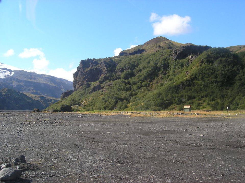 Rocky terrain with mountains and vegetation under a blue sky with clouds