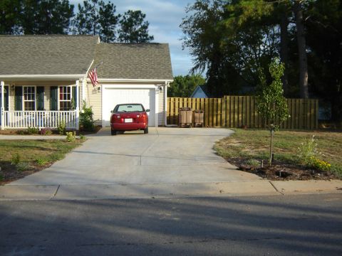 1986 Ford Bronco - A red sedan is parked in the driveway of a suburban home, with a wooden fence and trees in the background.