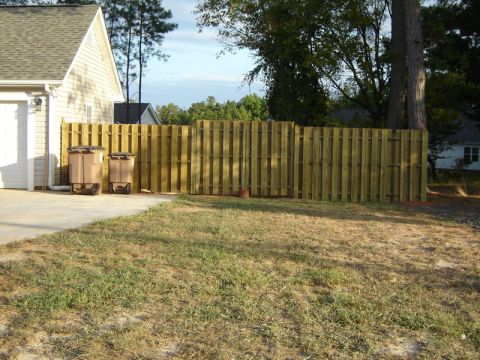 1986 Ford Bronco - Two trash cans sit on a concrete driveway beside a wooden fence, with a house and trees in the background.
