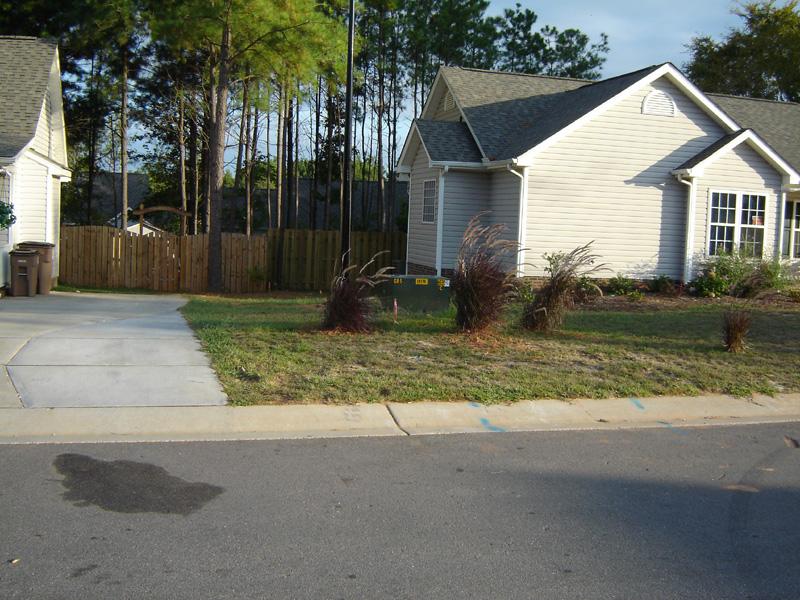 Residential house with a driveway, trash cans, and a patch of grass in front