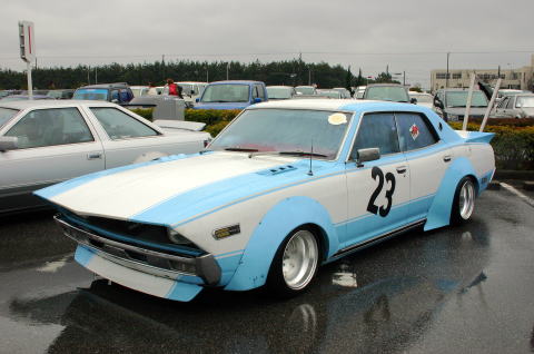 1991 Ford Bronco - A heavily modified sedan with a custom body kit and racing numbers sits in a wet parking lot.