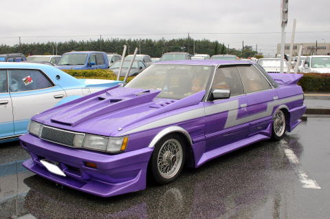 1991 Ford Bronco - A heavily customized purple sedan with a unique body kit and silver accents sits in a wet parking lot.