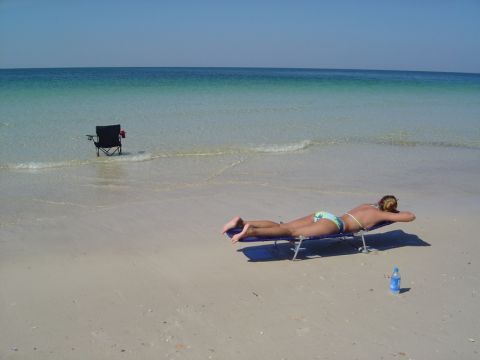 1986 Ford Bronco - A woman relaxes on a beach chair by the ocean, with another chair visible in the water.