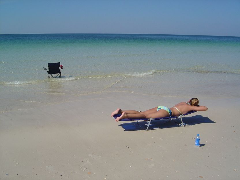 Woman sunbathing on a beach chair on a sandy beach with the ocean in the background