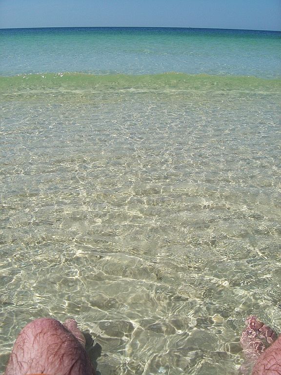 Feet in clear ocean water with a wave and horizon