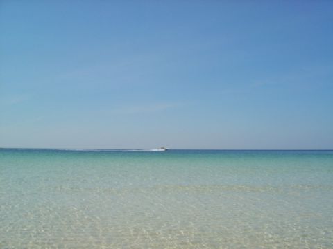 1986 Ford Bronco - A small boat travels across clear turquoise waters on a sunny day.