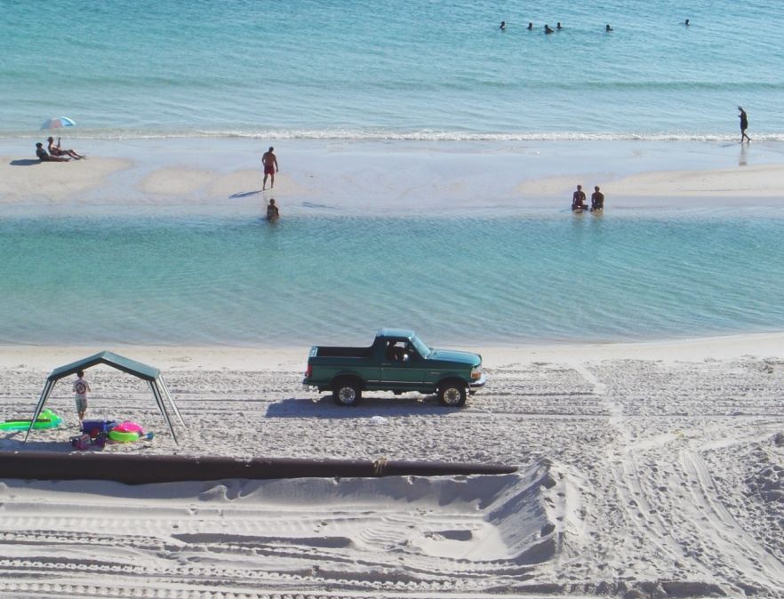 Dark green topless Ford SUV parked on white sand beach beside turquoise water