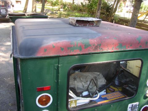 1973 Jeep CJ5 - A green Jeep CJ-5 hardtop shows peeling red paint on its roof and a vent. Gear is visible inside a storage compartment.