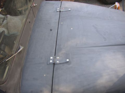 1973 Jeep CJ5 - Close-up view of the hood hinges and windshield frame of a dark-colored vehicle.
