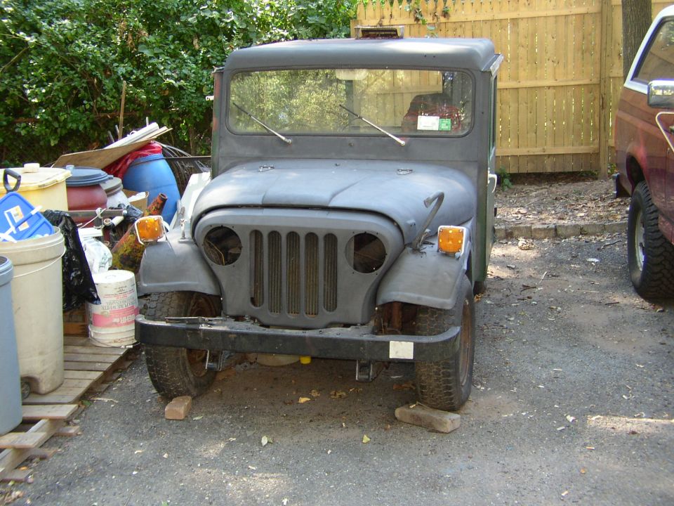 Gray Jeep truck with a flat grille and round headlights, parked on blocks