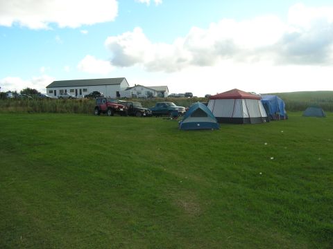 2001 Jeep Wrangler - Multiple vehicles, including a red Jeep Wrangler, are parked at a campsite with tents and buildings visible.