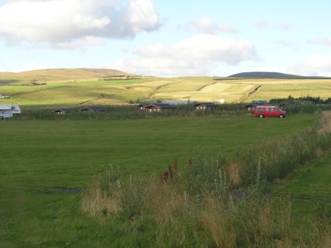 2001 Jeep Wrangler - A red van and RV are parked in a grassy field with cabins and rolling hills under a cloudy sky.