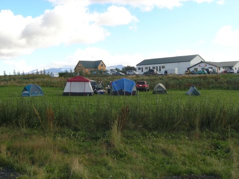 2001 Jeep Wrangler - Several tents are set up in a field with a red SUV and other vehicles parked nearby, along with buildings in the distance.