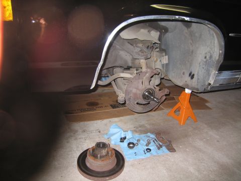 1991 Ford LTD Crown Victoria - car raised on an orange jack stand exposing the front brake rotor, with hub and brake parts laid out on the garage floor.