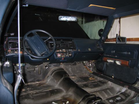 1991 Ford LTD Crown Victoria - Stripped car interior showing the dashboard and steering wheel with carpet removed exposing the bare metal floor pan.