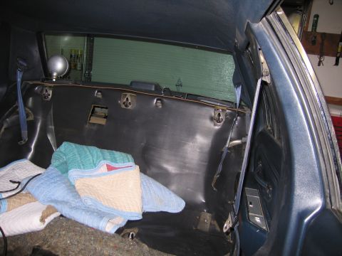 1991 Ford LTD Crown Victoria - Interior rear of a stripped car showing the bare parcel shelf and trunk partition with folded blankets on the floor.