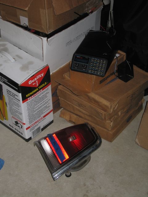 1991 Ford LTD Crown Victoria - red car tail light assembly resting on the floor beside cardboard boxes, a tools box, and a black electronic radio unit.