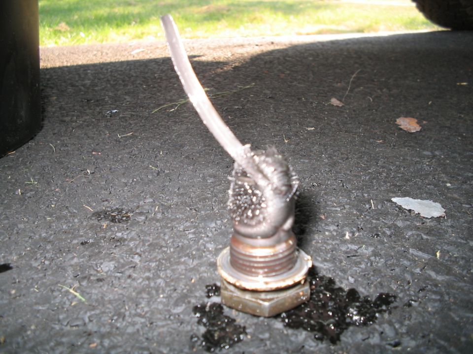 Sheared-off bolt or stud welded to a hex fitting on pavement under a vehicle