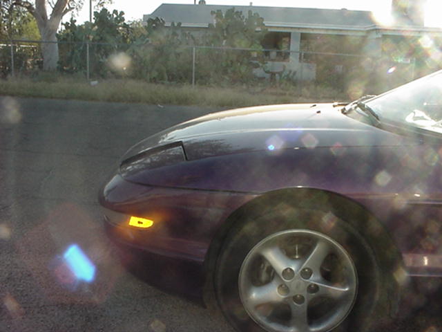 Dark purple Ford Probe front driver-side quarter with alloy wheel, chain-link fence and house behind