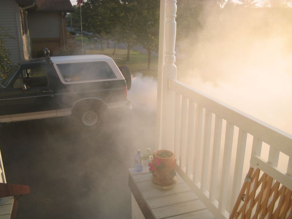 Ford Bronco with smoke coming out of exhaust, parked next to a house