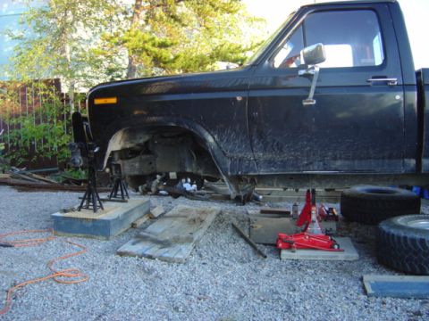 1986 Ford F-150 - A black pickup truck is elevated on jack stands, undergoing maintenance with its front wheel assembly exposed.