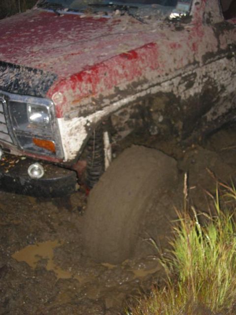 1985 Ford Bronco - This vehicle is deeply stuck in thick mud, with the front tire almost completely covered.