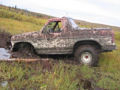 1985 Ford Bronco - This heavily mud-caked SUV appears to be from the early 1980s, stuck in a muddy ditch.