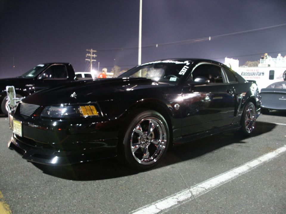 Black Ford Mustang with chrome rims parked at night. Another truck is to the left