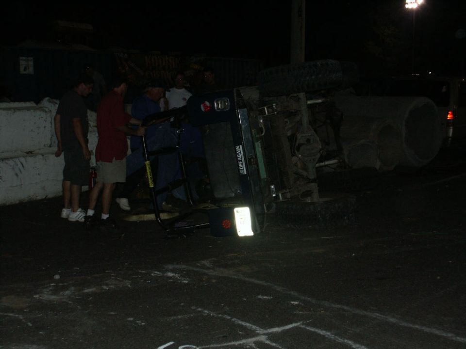 Overturned dark-colored vehicle on its side with people around it at night