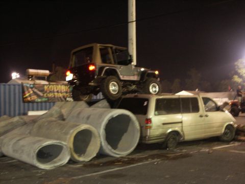 2001 Mercury Grand Marquis - A Jeep Wrangler is positioned precariously on top of a van, with concrete pipes in the foreground.