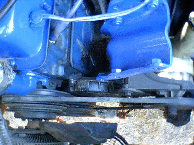 Close-up of engine components, some painted bright blue. Belts and pulleys are visible
