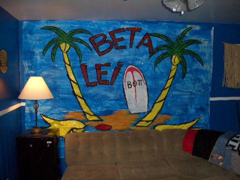 1990 Ford Bronco - A wall mural depicts a tropical beach scene with palm trees and a surfboard, likely a fraternity or sorority decoration.